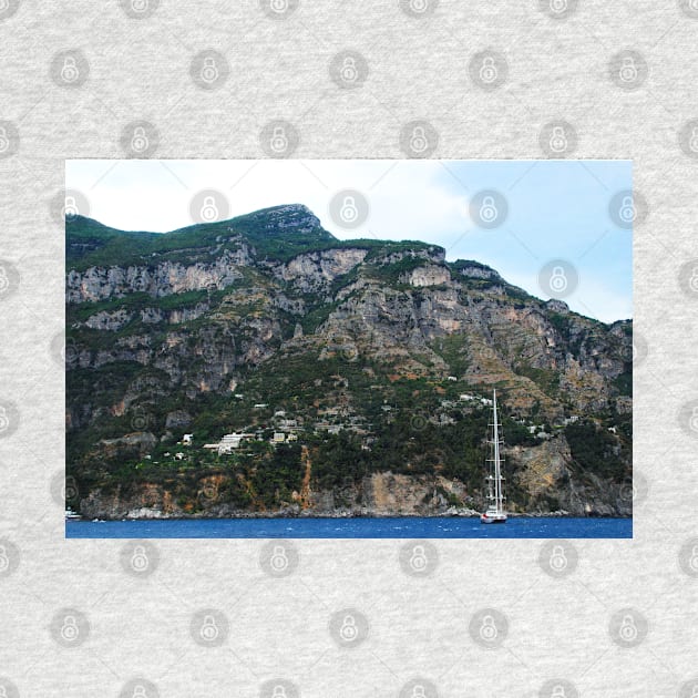 View in Amalfi coast at a huge mountain with rocky parts, greenery and buildings with a white boat underneath by KristinaDrozd